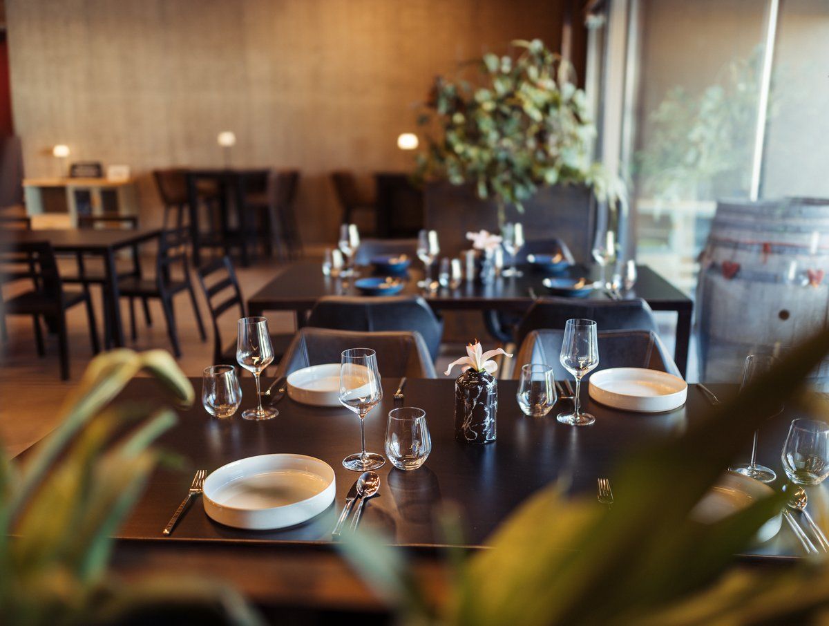 Elegantes Restaurant mit gedeckten Tischen, Weingläsern und Pflanzen im Hintergrund.