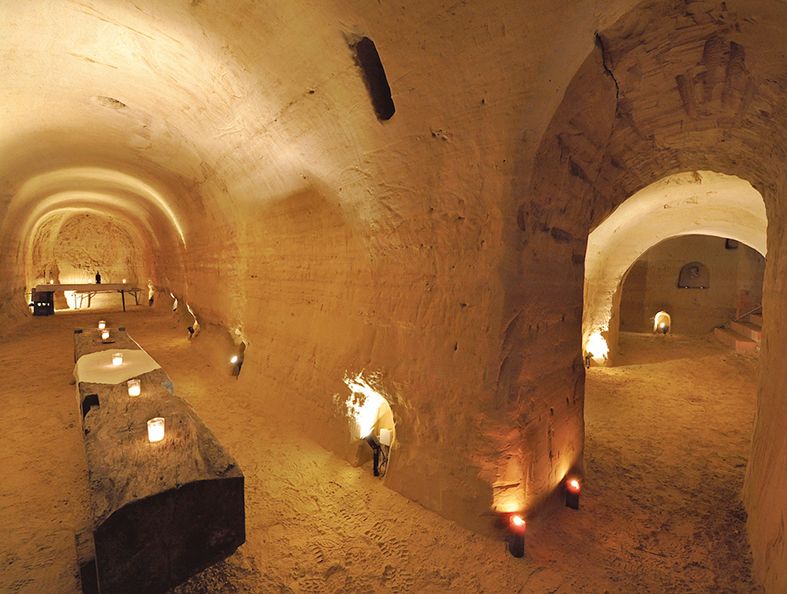 Unterirdischer Sandsteinkeller mit Kerzenlicht und rustikalen Tischen.