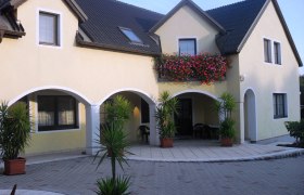Ein gelbes Haus mit dunklem Dach, Balkon mit Blumen und Pflanzen im Hof.