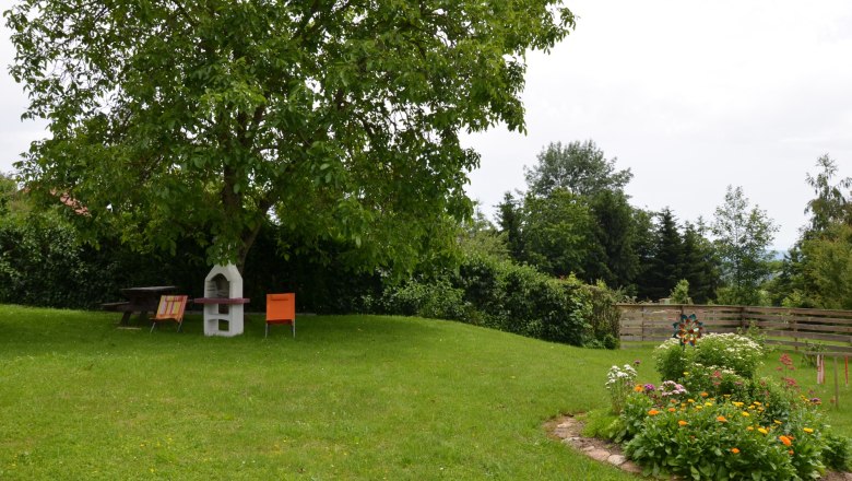 Ein gr&uuml;ner Garten mit einem Baum, Gartenm&ouml;beln und Blumenbeet.