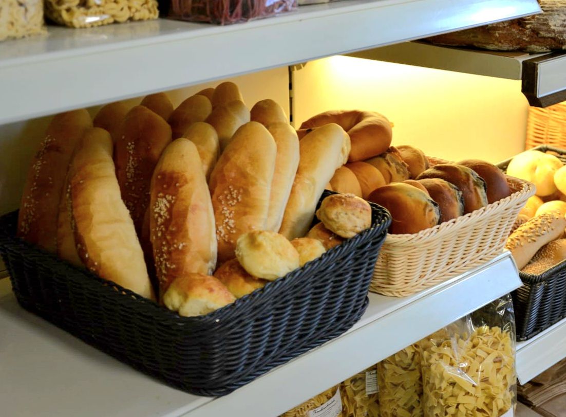 Regal mit verschiedenen Brotsorten in Körben, darunter Baguettes und Brötchen.