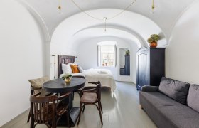 Ein stilvoll eingerichtetes G&auml;stezimmer mit gew&ouml;lbter Decke, Bett, Sofa, Tisch und St&uuml;hlen. Ein Fenster l&auml;sst Tageslicht herein.