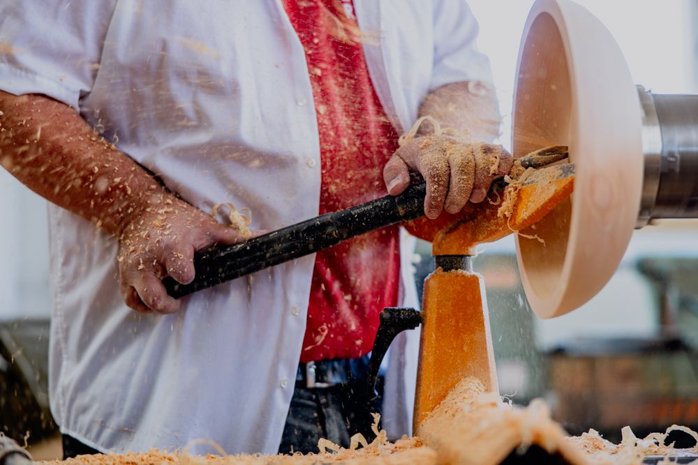 Person drechselt Holz auf einer Drechselbank, Späne fliegen.