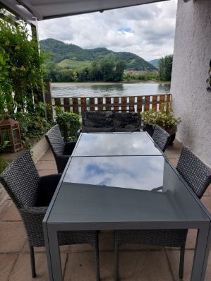 Terrasse mit Tisch und Stühlen, Blick auf Fluss und Hügel.