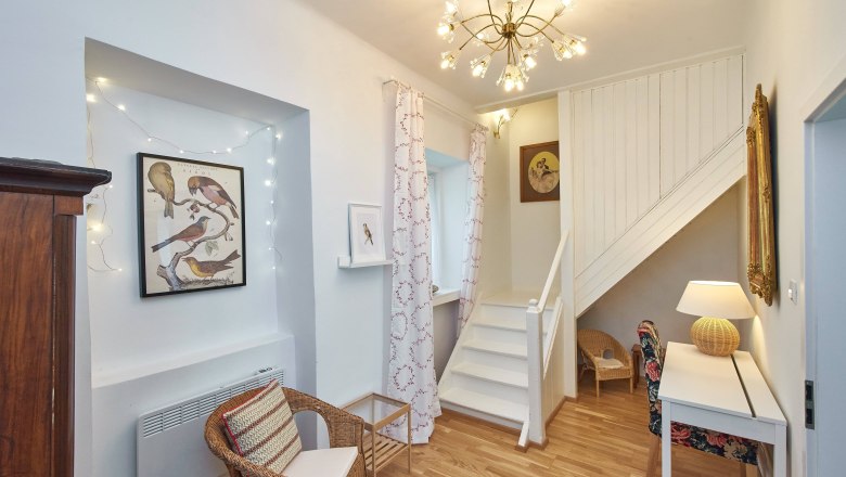 Wohnbereich mit Treppe, Rattanm&ouml;beln und Vogelbildern an der Wand.