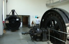 Innenansicht eines Schaukraftwerks mit großen Turbinen und einer Person, die eine Informationstafel liest.