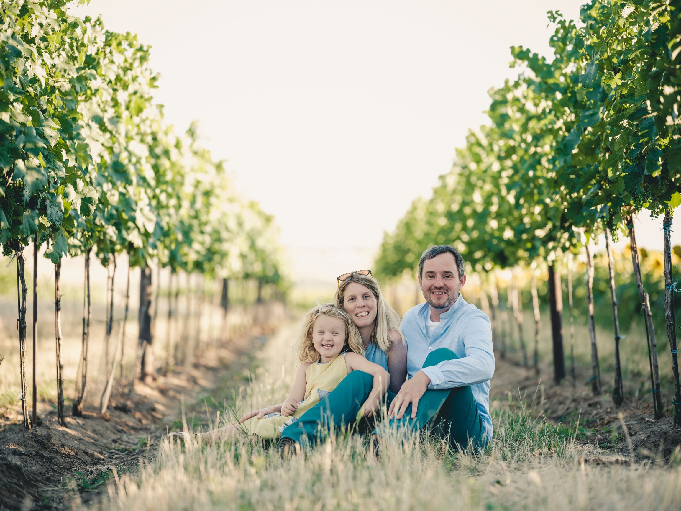 Familie sitzt zwischen Weinreben in einem Weinberg.