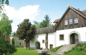 Ein traditionelles Geb&auml;ude mit Holzdach und wei&szlig;er Fassade, umgeben von einem gr&uuml;nen Garten.