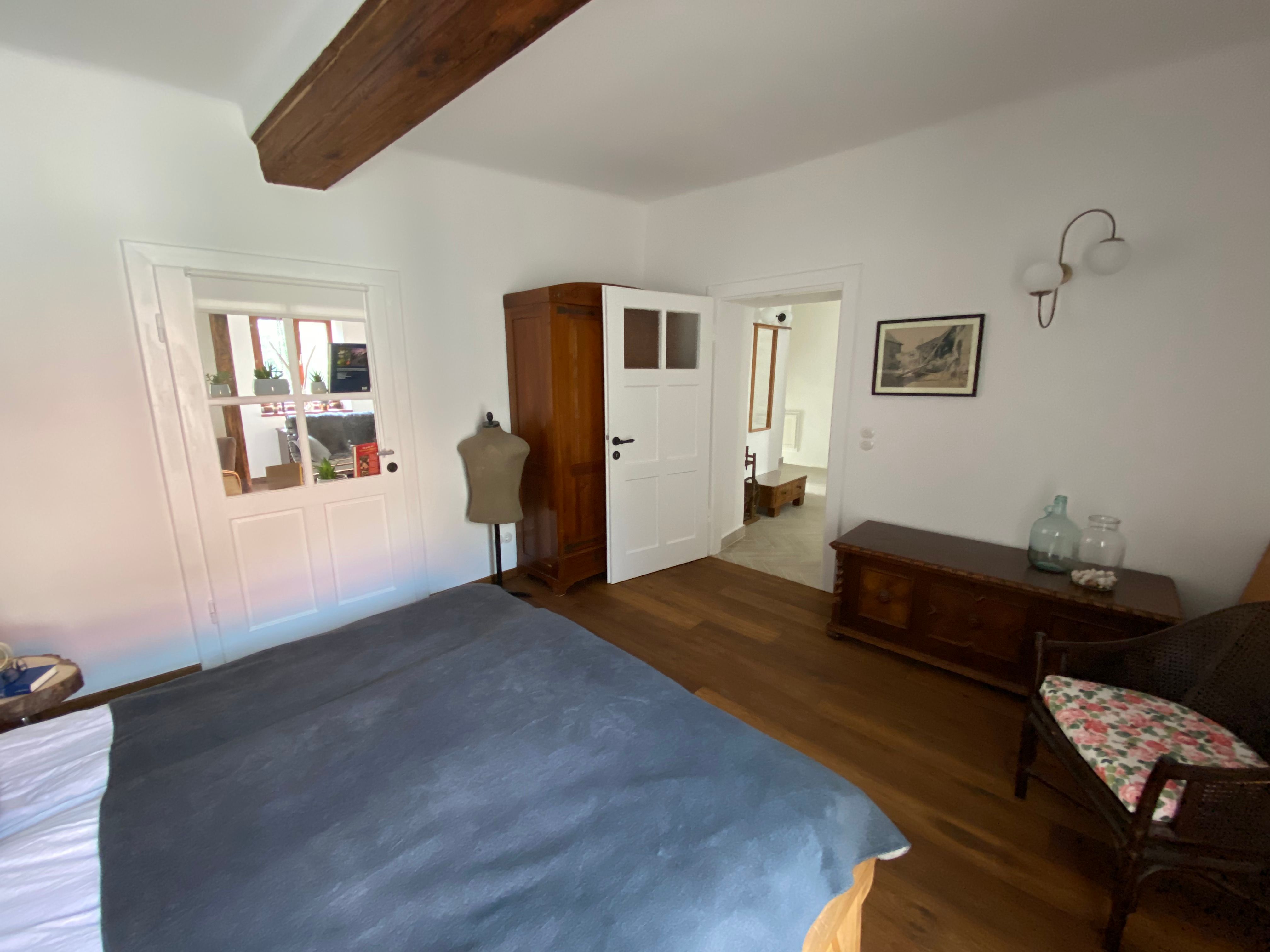 Schlafzimmer mit Holzboden, Bett, Kleiderschrank, Kommode und Stuhl.