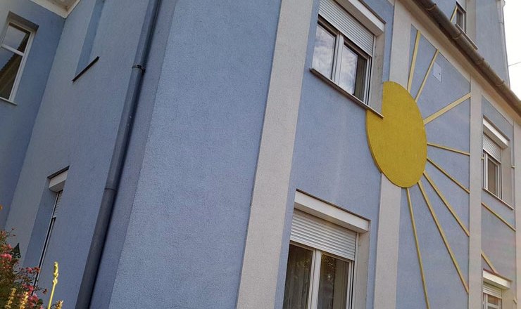 Blaues Haus mit gelber Sonnendekoration an der Fassade.