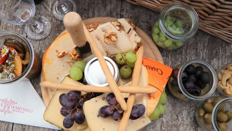 Käseplatte mit Trauben, Nüssen und Brotstangen auf einem Holztisch.