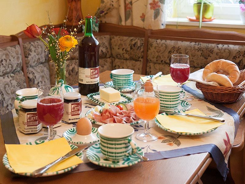 Ein gedeckter Frühstückstisch mit Brötchen, Marmelade, Eiern, Saft und Blumen.