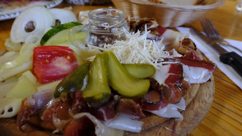 Eine rustikale Platte mit Wurst, Käse, Gurken und Tomaten auf einem Holztisch.