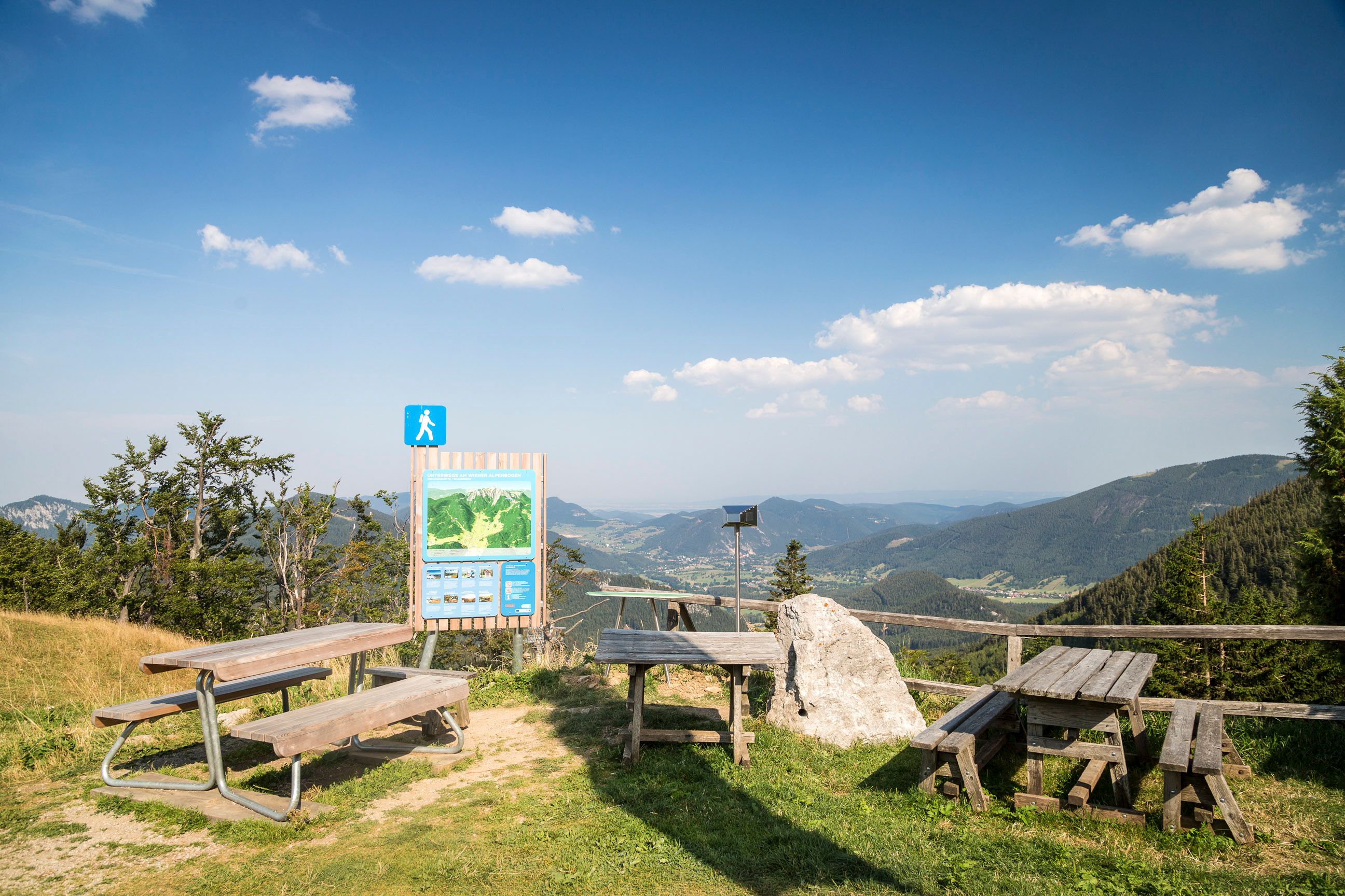 Aussichtspunkt mit Holzbänken und Infotafel in den Bergen.