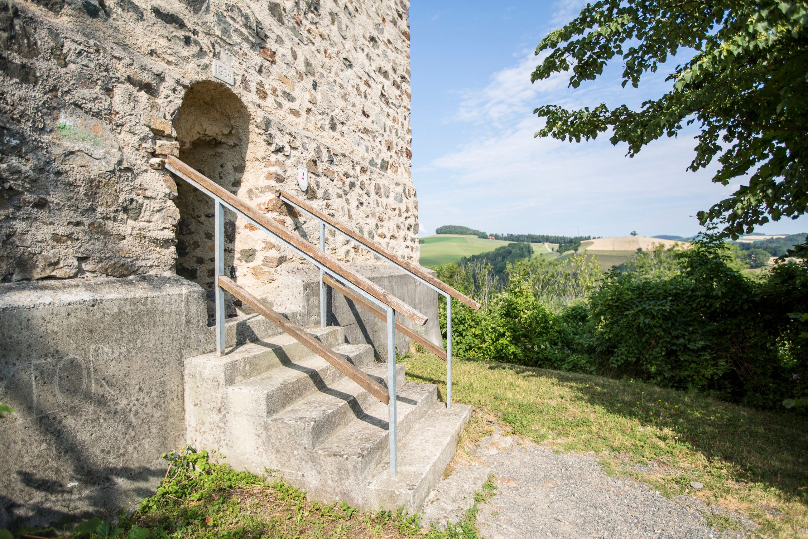 Eingang zum Feuerturm der Burgruine Kirchschlag mit Treppe und Landschaft im Hintergrund.