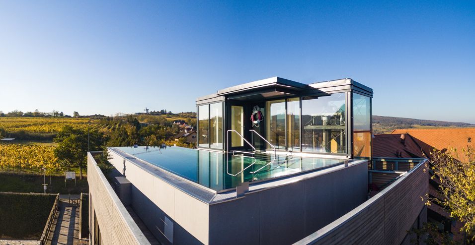 Dachpool mit Glaswänden auf einem Gebäude, umgeben von herbstlicher Landschaft und Weinbergen.