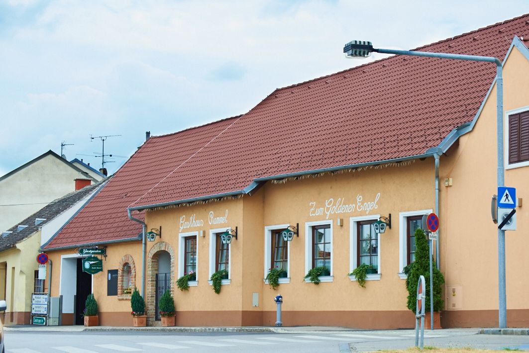 Ein traditionelles Gasthaus mit gelber Fassade und rotem Dach, beschriftet mit 'Gasthaus Rammel' und 'Zum Goldenen Engel'.