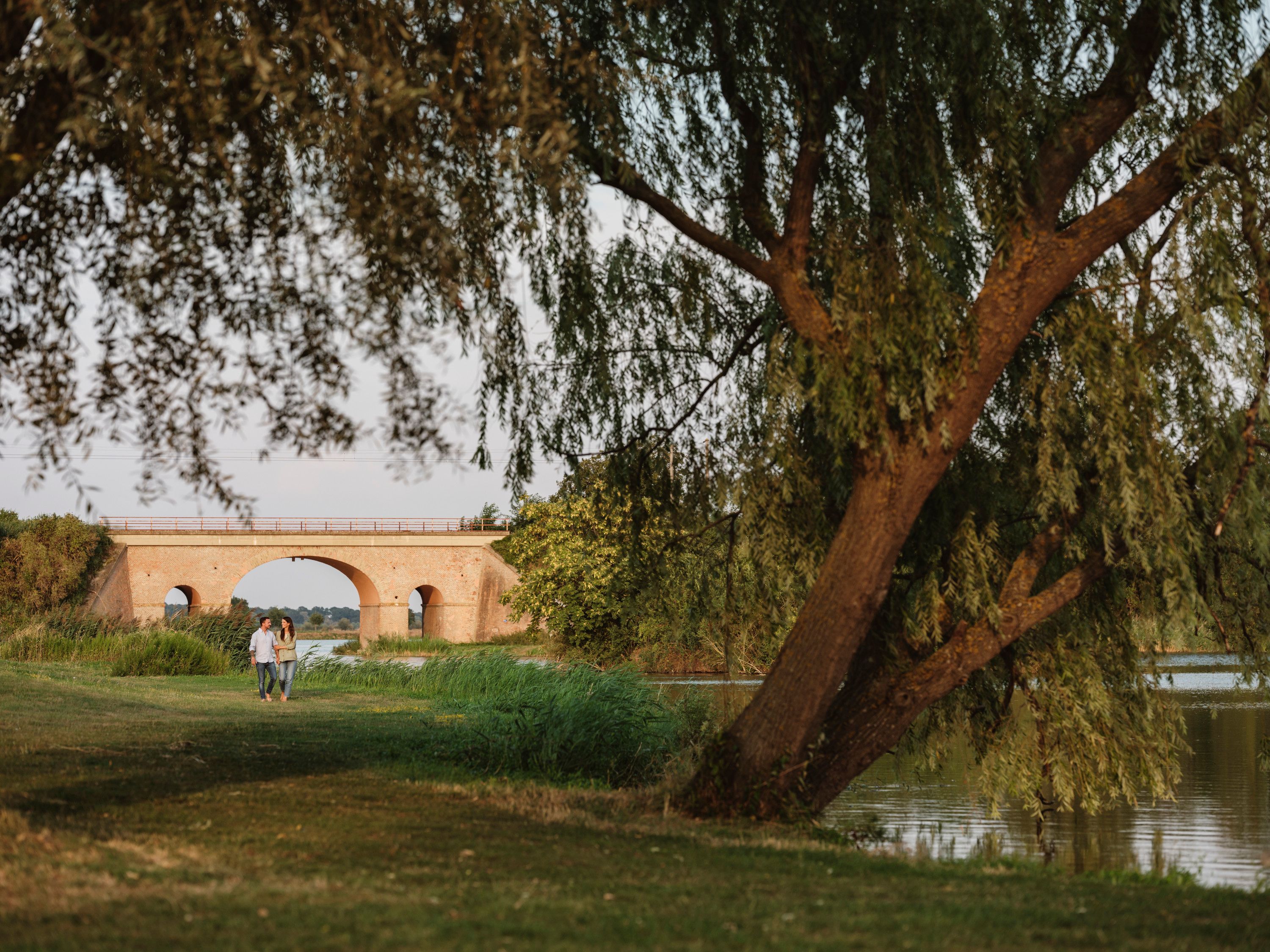 Paar spaziert an einem Teich mit Brücke im Hintergrund.