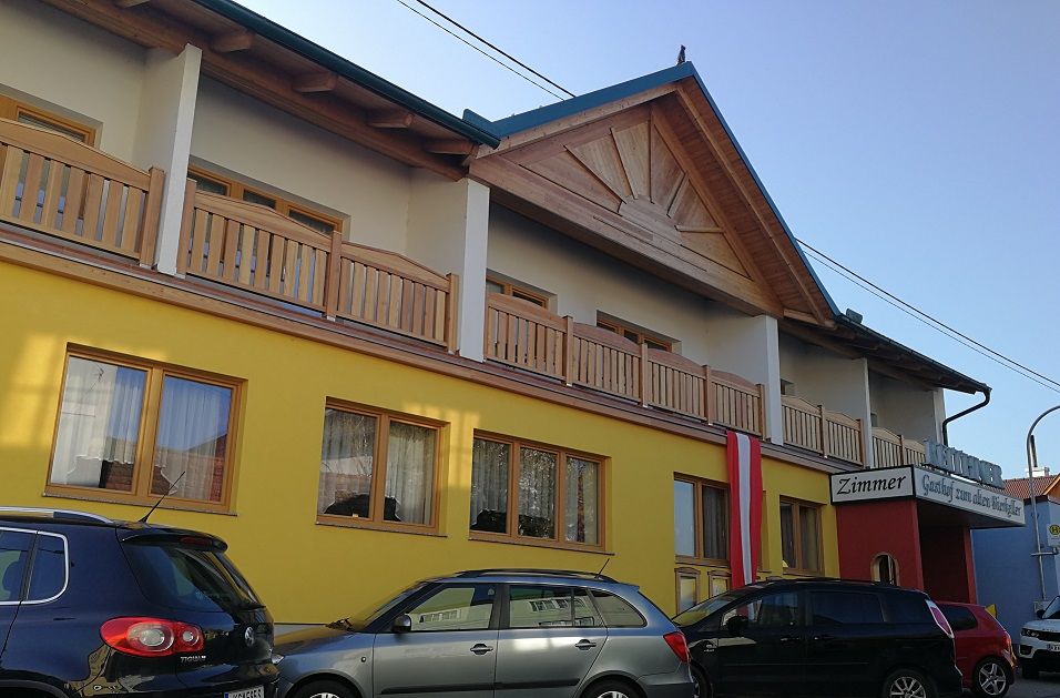 Außenansicht eines gelben Gebäudes mit Holzveranda und Autos davor.