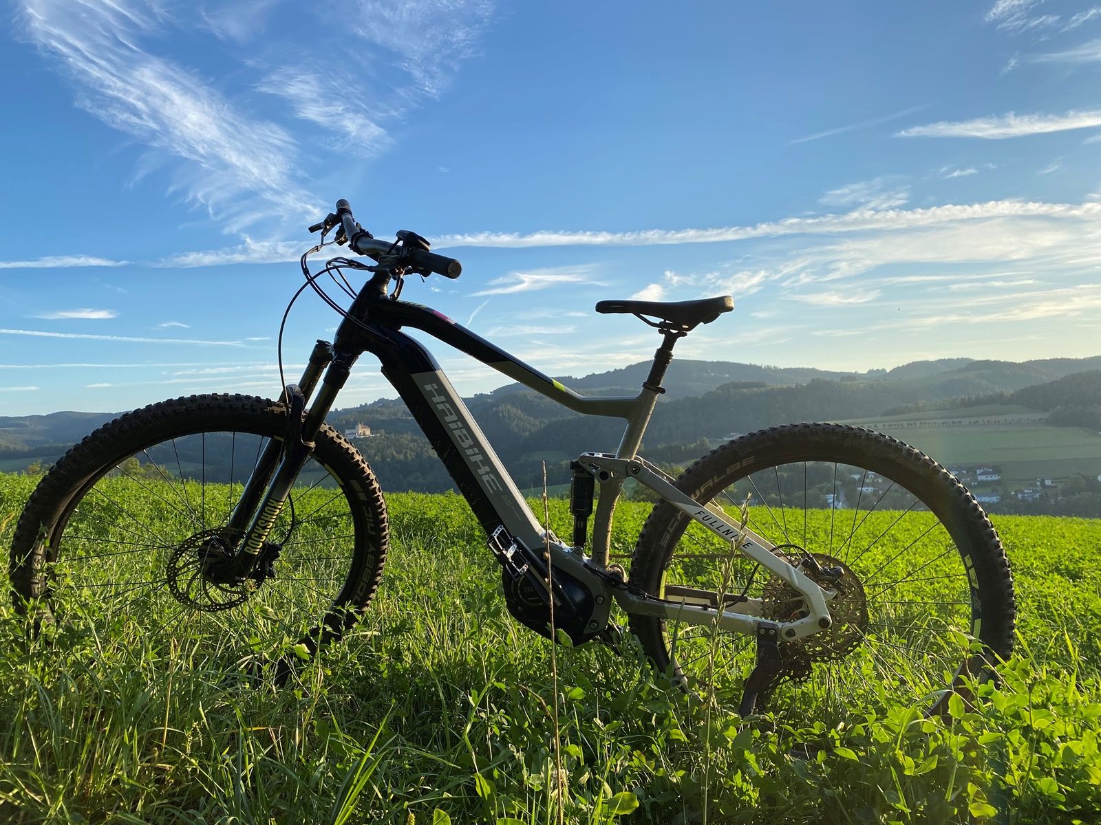 Nahaufnahme eines Fahrrads auf grüner Wiese mit Hügellandschaft im Hintergrund.