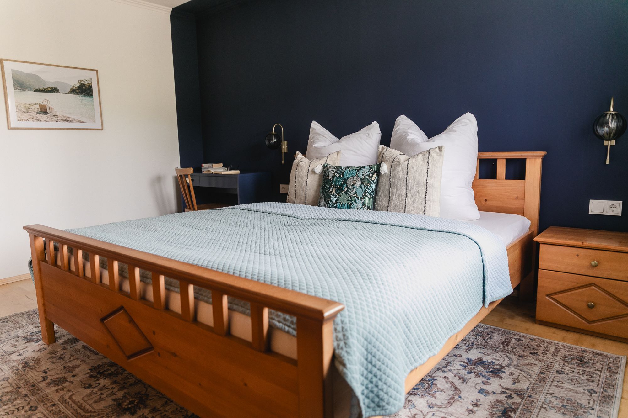 Gemütliches Schlafzimmer mit Holzbett, blauer Wand und dekorativen Kissen.