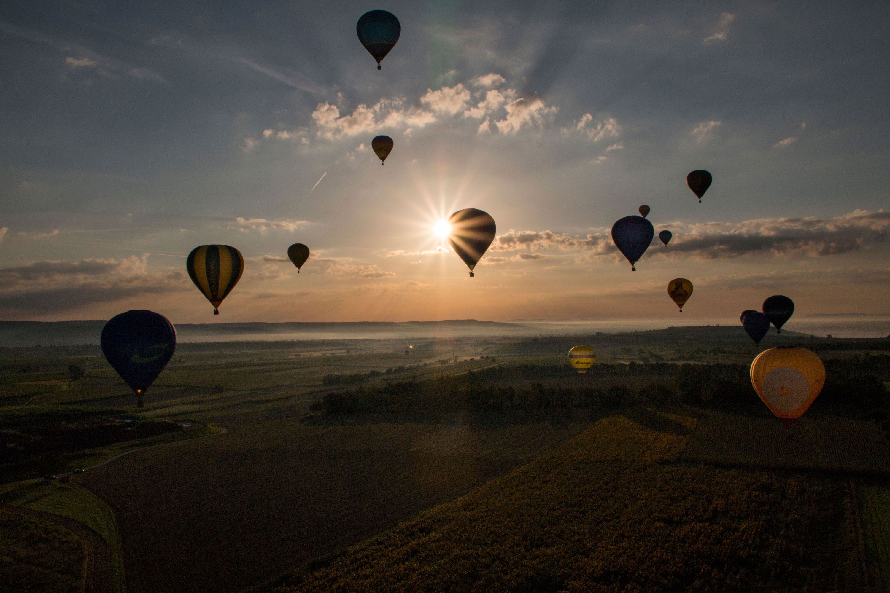 Heißluftballons schweben bei Sonnenaufgang über eine Landschaft.