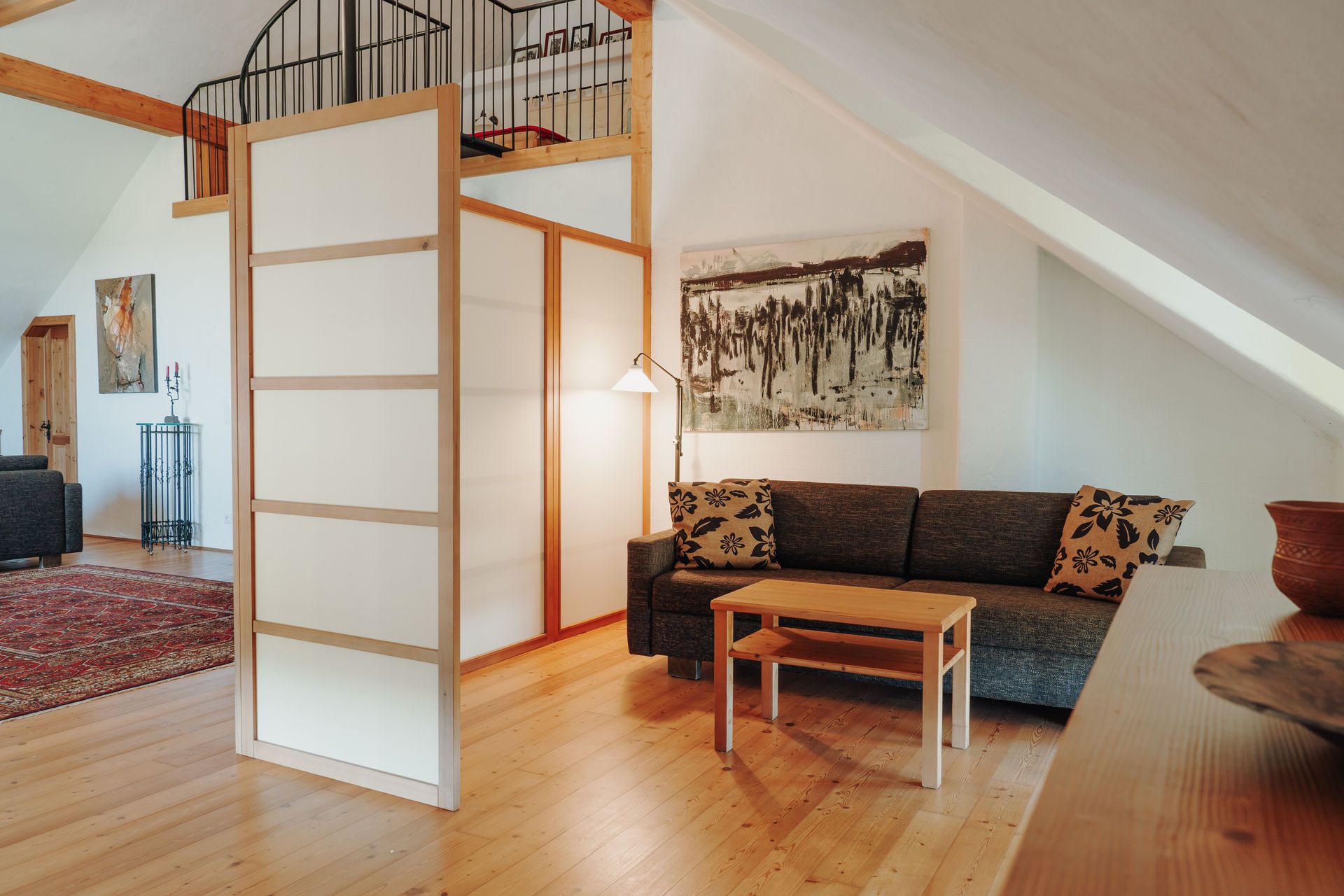 Gemütliche Sitzecke mit Sofa, Couchtisch und Raumteiler in einem Dachgeschosszimmer.