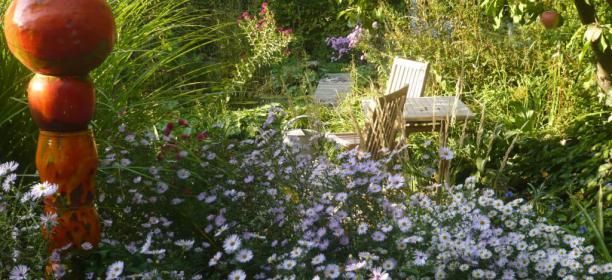 Ein blühender Garten mit violetten Blumen, einem Holztisch und Stühlen im Hintergrund.