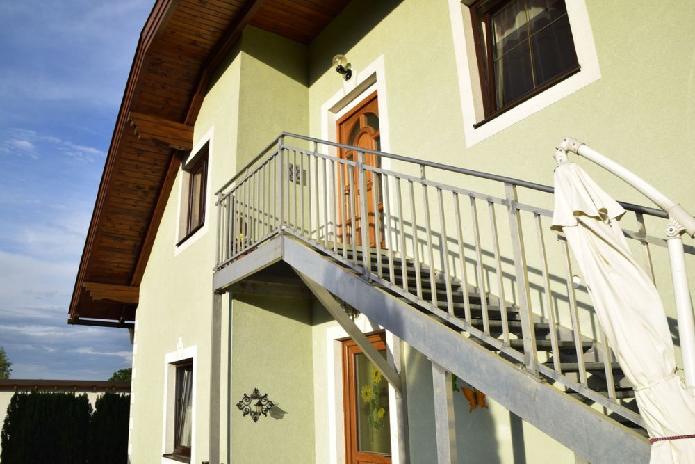 Außentreppe eines grünen Hauses mit Holzdach und Sonnenschirm.