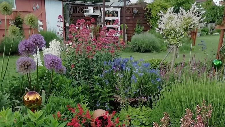 Ein &uuml;ppiges Staudenbeet mit bunten Blumen und Dekorationen in einem Garten.