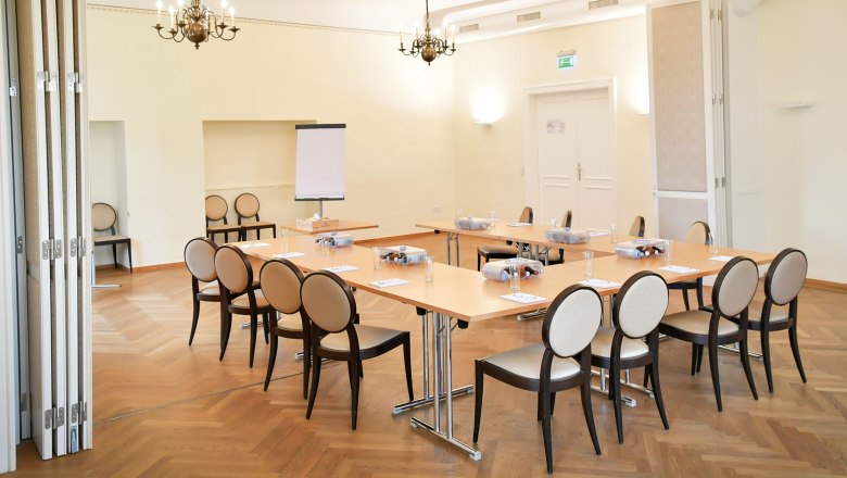 Konferenzraum mit Tischen und Stühlen, Flipchart und Kronleuchter.