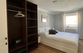 Modernes Schlafzimmer mit Doppelbett, Kleiderschrank und Fenster mit Vorh&auml;ngen.