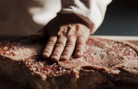 Nahaufnahme einer Hand, die grobes Salz auf ein großes Stück rohes Fleisch streut.