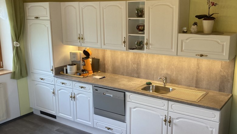 K&uuml;che mit wei&szlig;en Schr&auml;nken, Geschirrsp&uuml;ler und Sp&uuml;le.