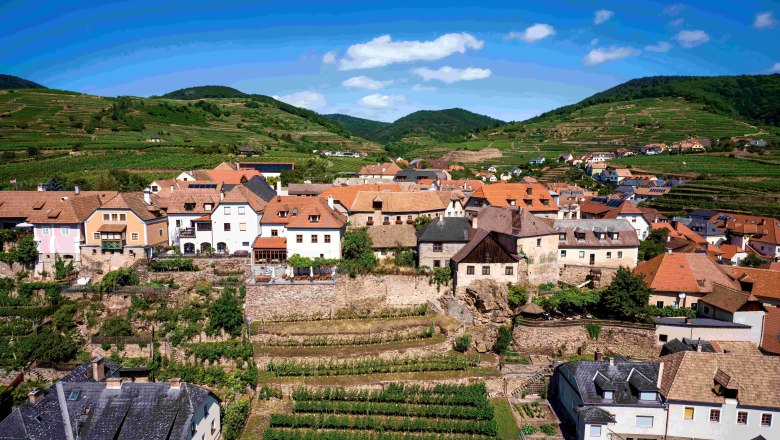 Ansicht von Wei&szlig;enkirchen mit dem Ortsteil Burg mit zahlreichen H&auml;usern, einem Weing&auml;rten und H&uuml;geln im Hintergrund