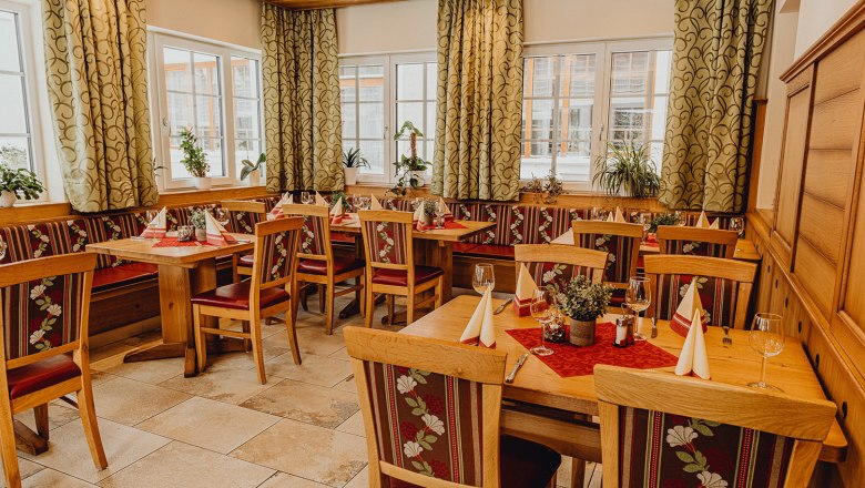 Gemütliches Restaurant mit Holzmöbeln, dekorierten Tischen und Pflanzen am Fenster.