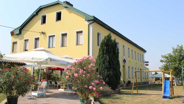 Gelbes Geb&auml;ude mit Terrasse und Spielplatz im Vordergrund.