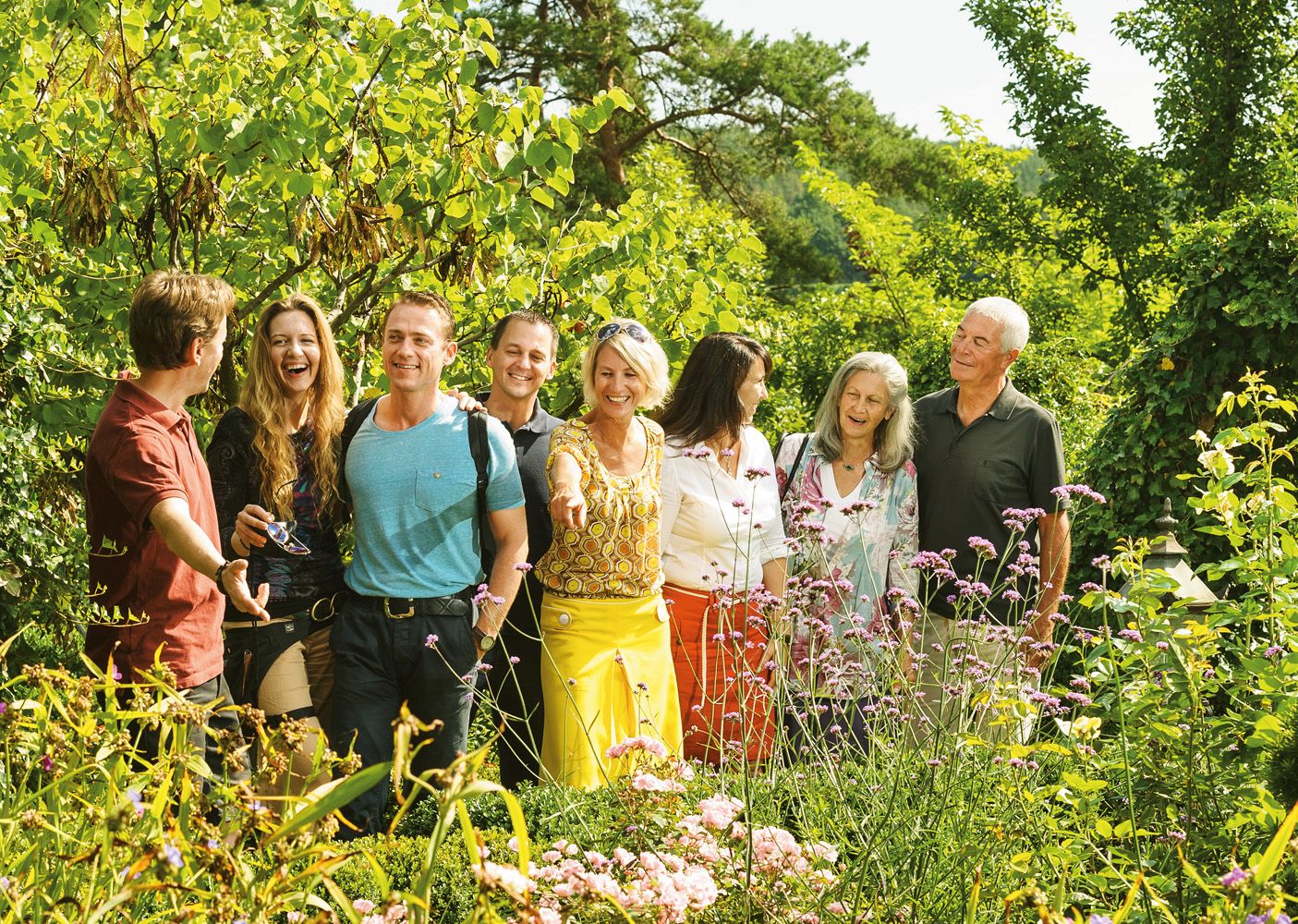 Eine Gruppe von Menschen steht lächelnd in einem blühenden Garten.