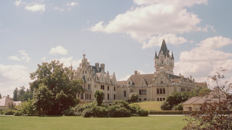 Schloss Grafenegg mit weitl&auml;ufigem Rasen und B&auml;umen im Vordergrund.