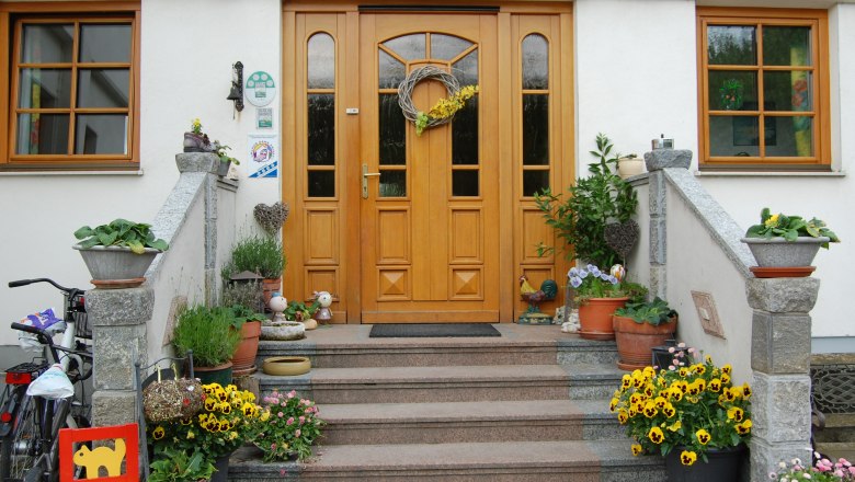Vorderseite eines Hauses mit Holzt&uuml;r, Treppe und Blumendekoration.