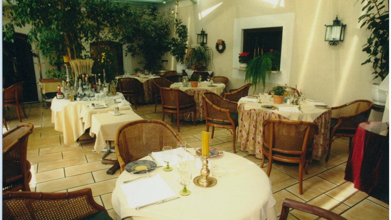 Ein gemütlicher Wintergarten eines Landhotels mit gedeckten Tischen, Pflanzen und Korbstühlen.