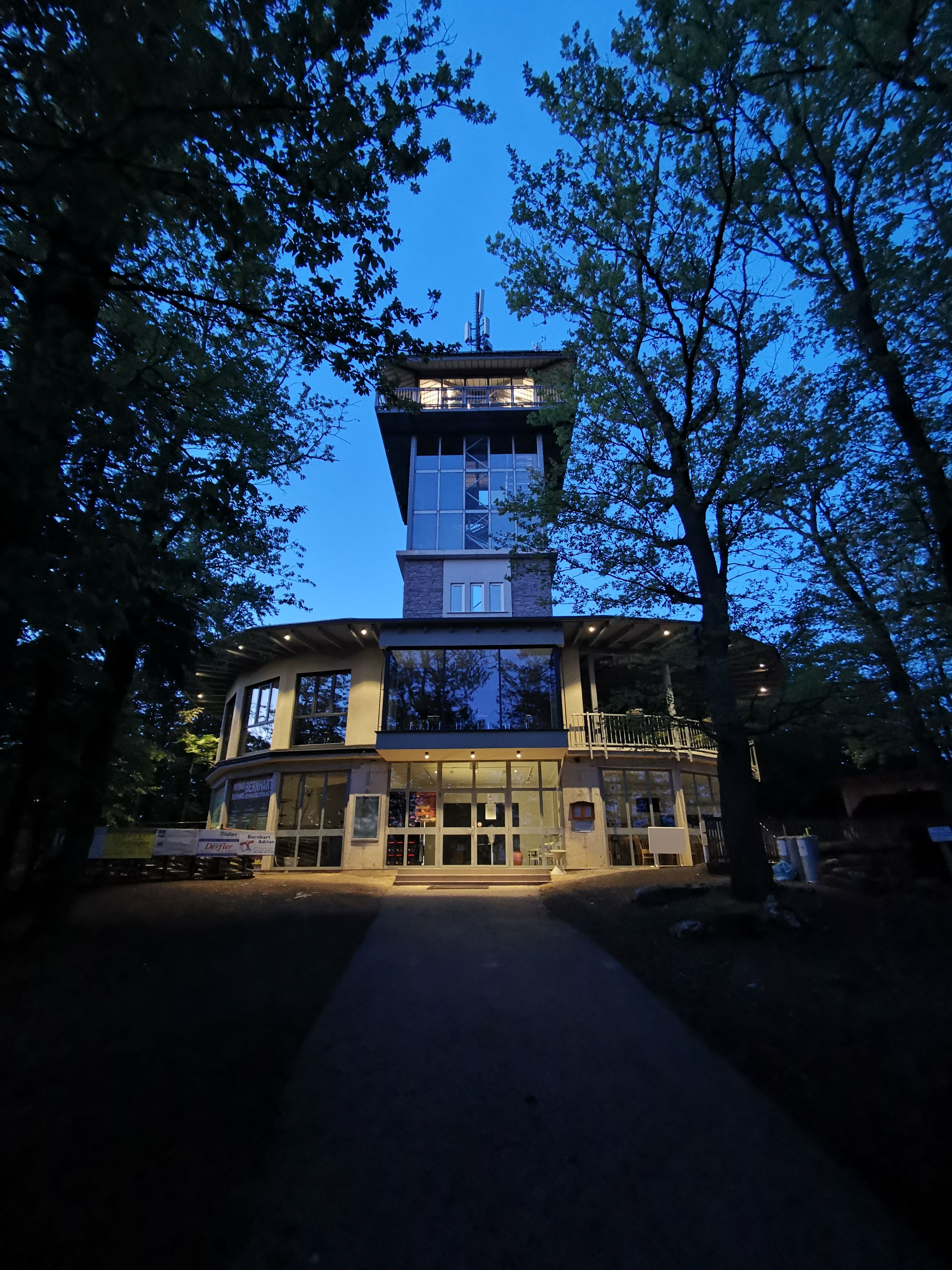 Ovales Gebäude mit Aussichtsturm aus Glas bei Nacht.