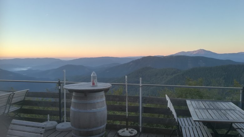 Terrasse mit Holzm&ouml;beln und Bergblick bei Sonnenaufgang.
