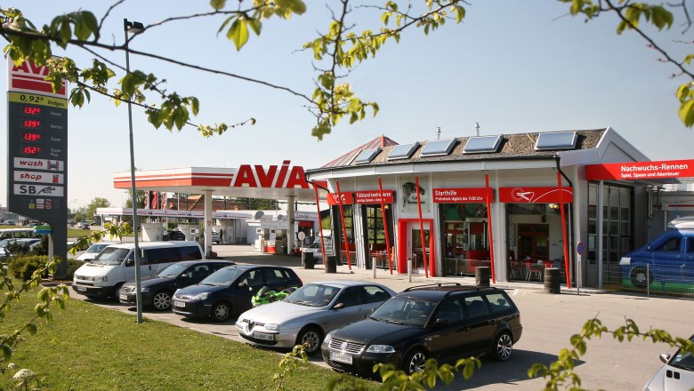 Tankstelle mit AVIA-Logo und mehreren geparkten Autos im Vordergrund.