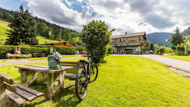 Ein Fahrrad steht neben einem Picknicktisch auf einer grünen Wiese vor einem Gebäude namens Hubertushof.
