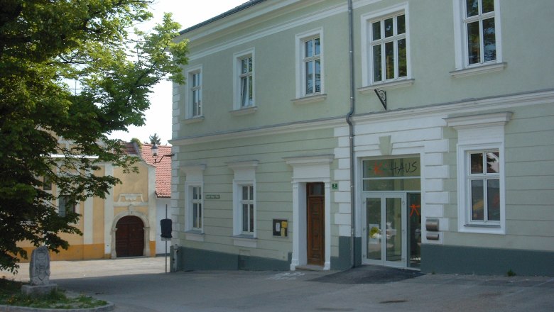 Ein zweist&ouml;ckiges, hellgr&uuml;nes Geb&auml;ude mit der Aufschrift 'Haus' &uuml;ber der T&uuml;r.