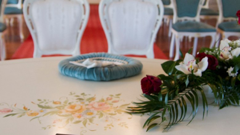 Ein eleganter Raum mit wei&szlig;en St&uuml;hlen und einer Trauungsmappe auf einem Tisch.