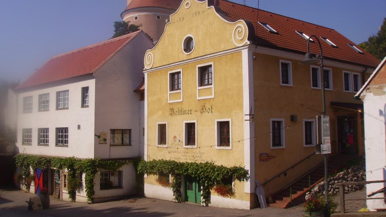 Historisches Gebäude mit gelber Fassade und roten Dachziegeln, daneben ein weißes Gebäude. Im Hintergrund ein Turm mit Kuppel.