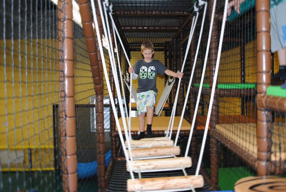 Ein Junge balanciert auf einer Hängebrücke in einem Indoor-Klettergarten.