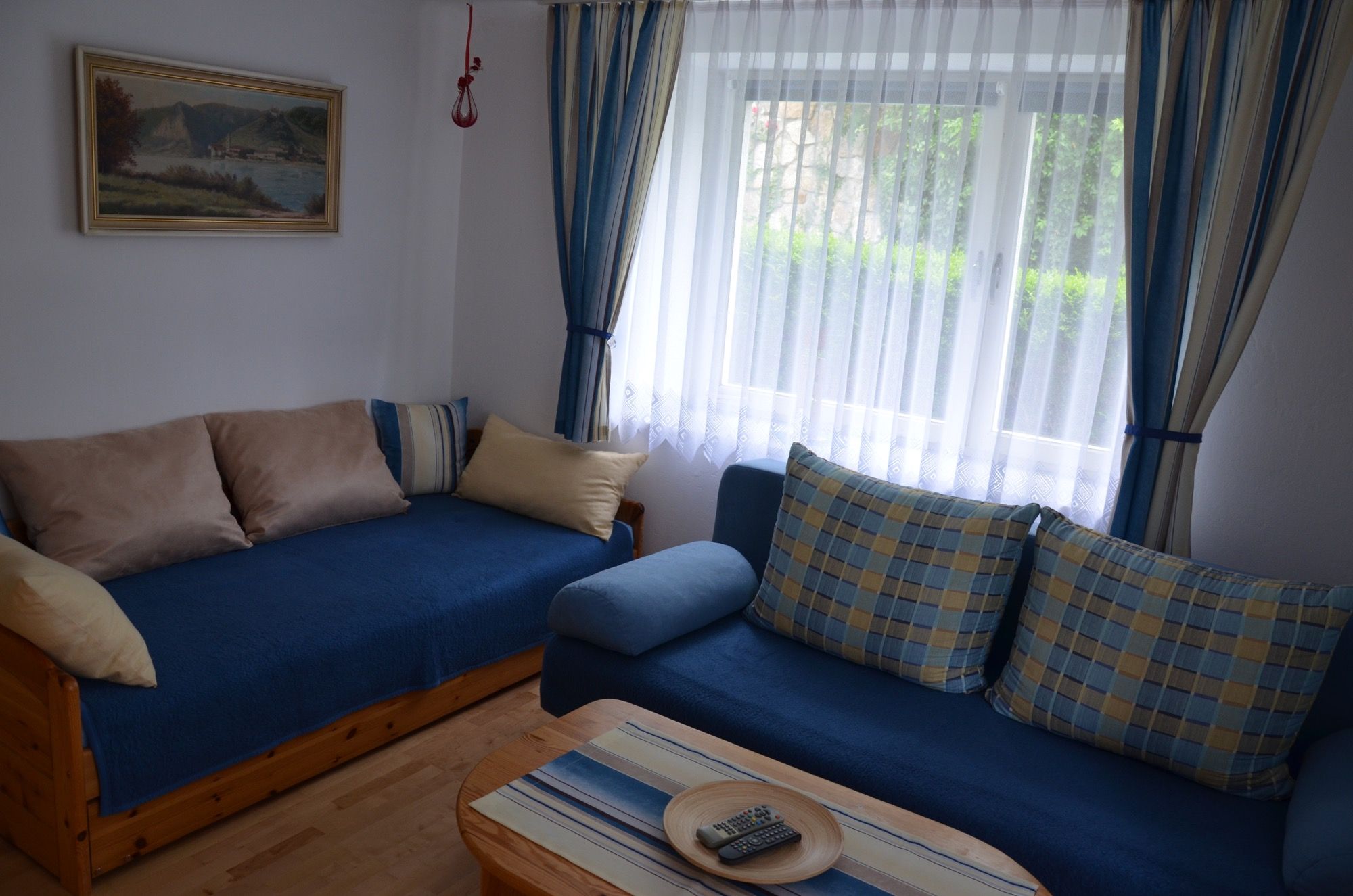 Gemütliches Wohnzimmer mit blauen Sofas, Kissen, einem Holztisch und einem Fenster mit Vorhängen.